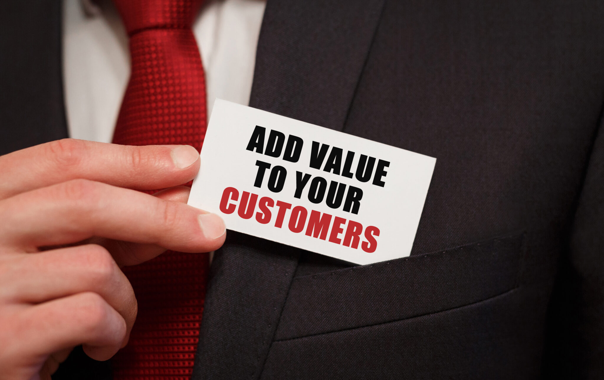 Businessman putting a card with text ADD VALUE TO YOUR CUSTOMERS in the pocket